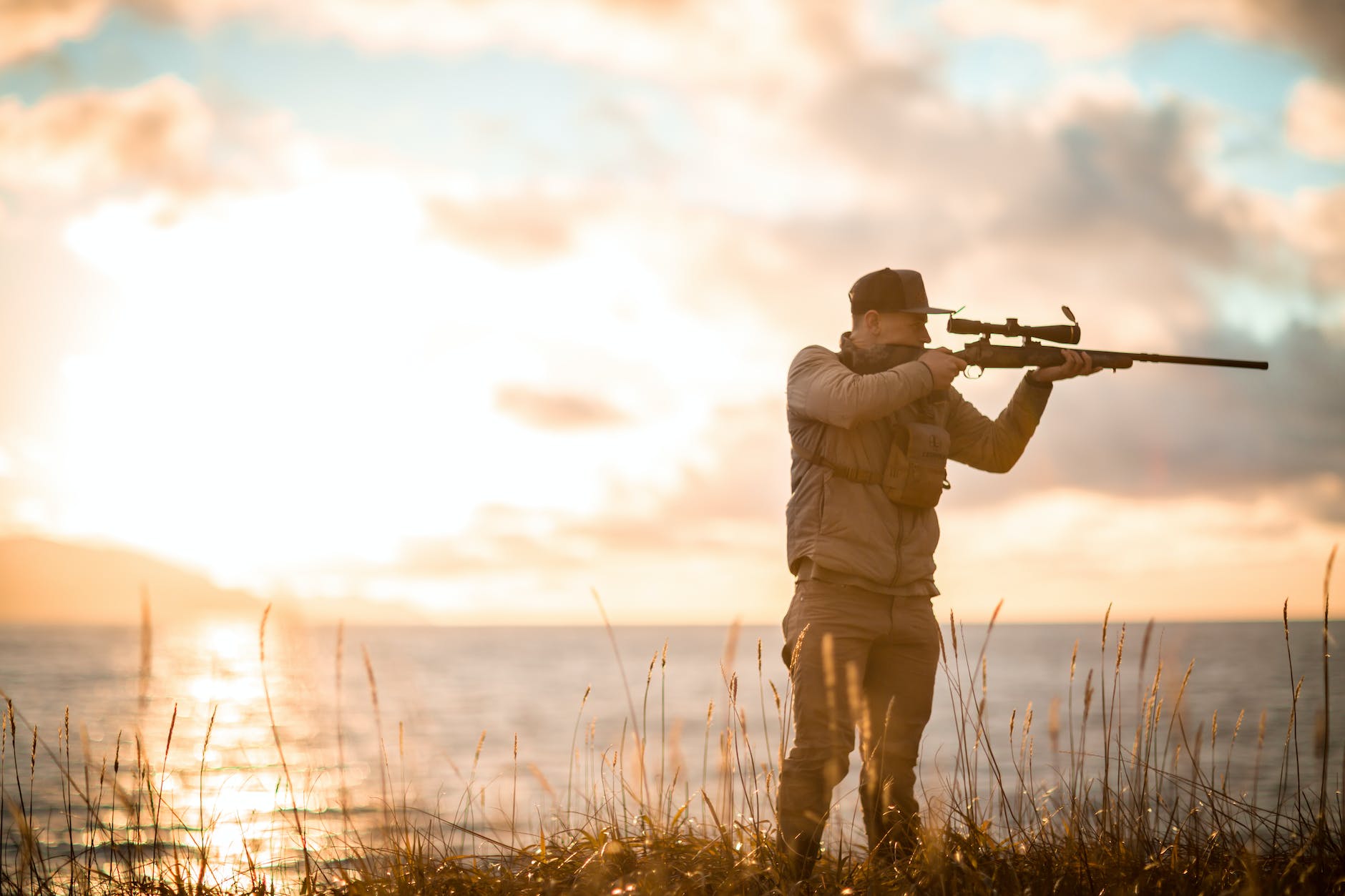 man aiming with sniper rifle on sea shore